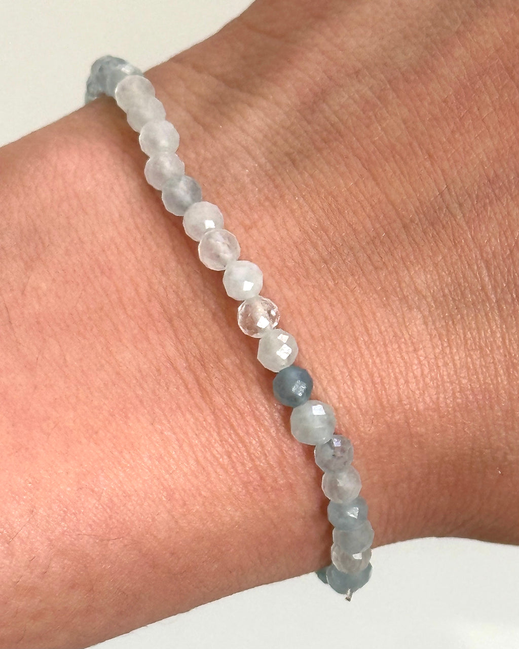 A beaded bracelet made of pale translucent white and light blue faceted beads worn on a person's wrist.
