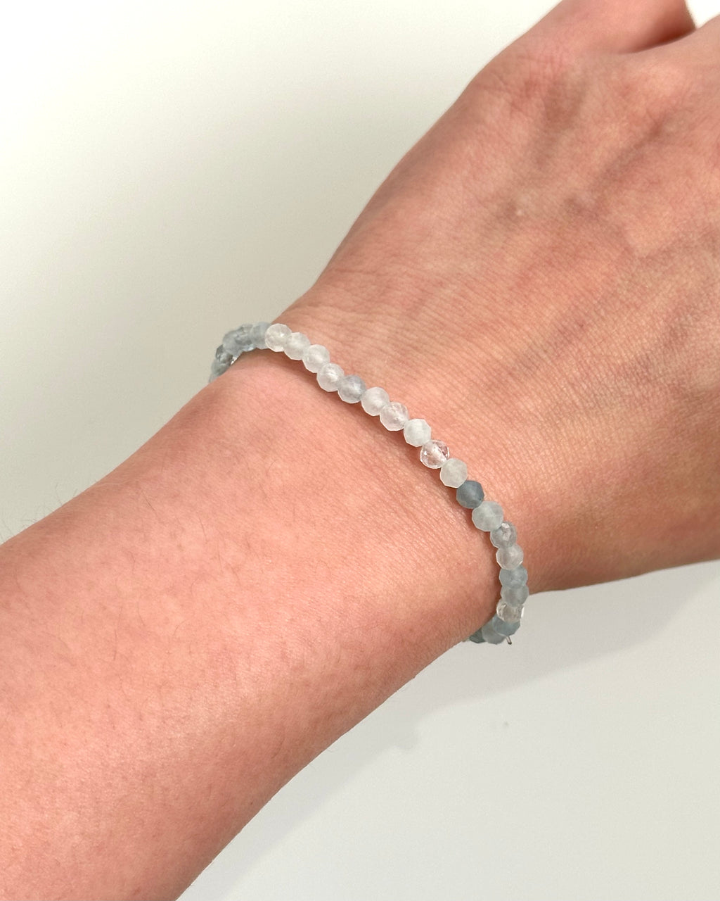 A beaded stretch bracelet made of translucent pale gray and white round beads, shown worn on a person's wrist against a plain light background.