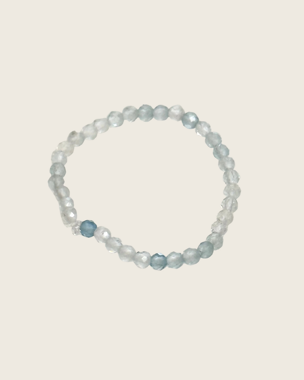 A beaded stretch ring featuring translucent light blue and frosted white faceted beads, with one prominent faceted light blue bead near the bottom left of the ring, displayed on a plain off-white background.