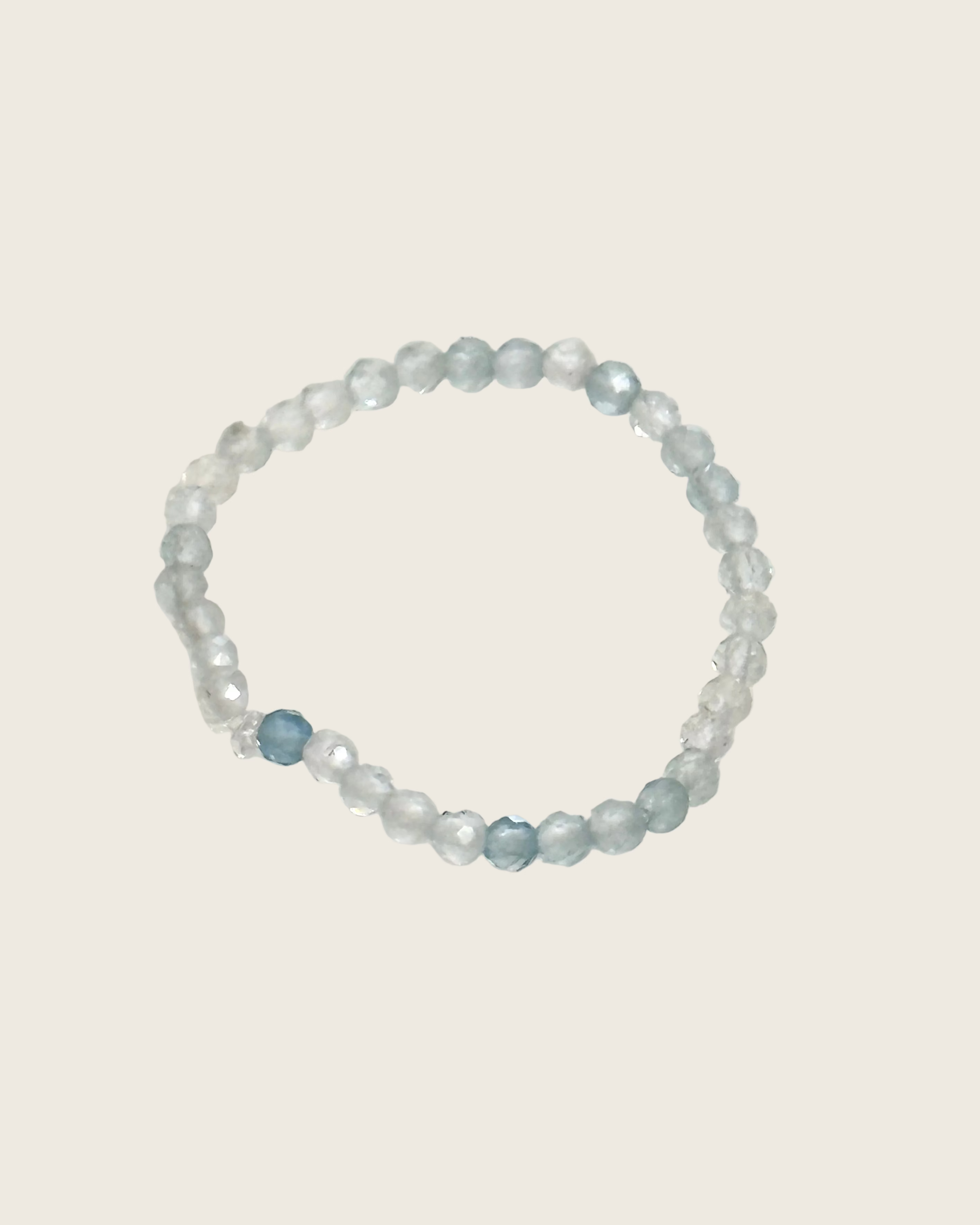 A beaded stretch ring featuring translucent light blue and frosted white faceted beads, with one prominent faceted light blue bead near the bottom left of the ring, displayed on a plain off-white background.