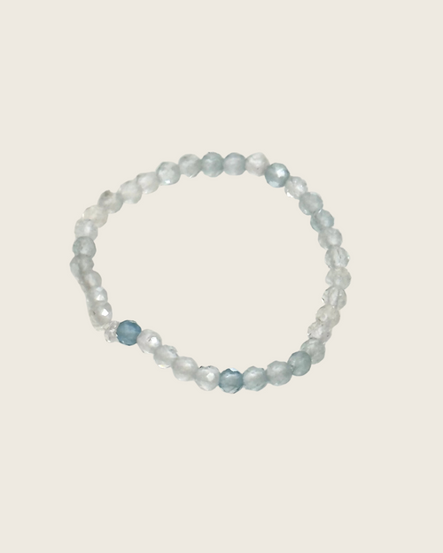 A beaded stretch ring featuring translucent light blue and frosted white faceted beads, with one prominent faceted light blue bead near the bottom left of the ring, displayed on a plain off-white background.