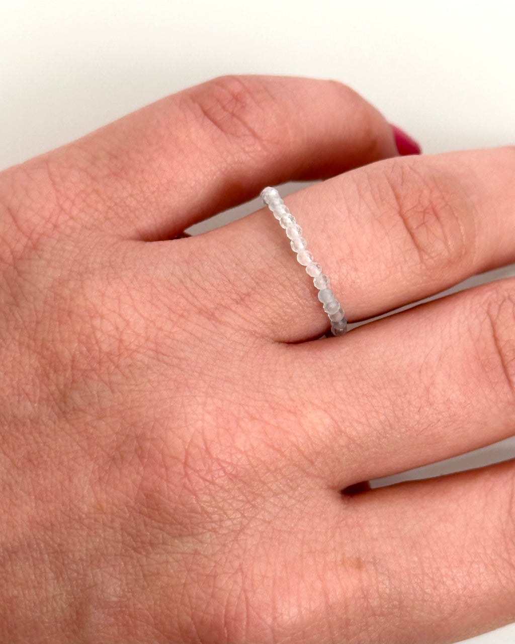 A close-up of a hand wearing a delicate, thin beaded ring on one finger.