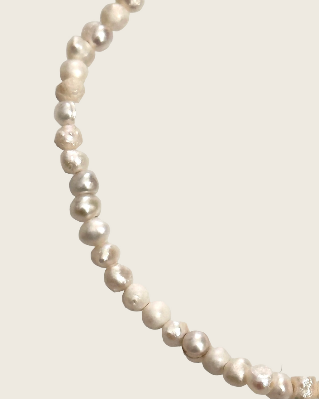 A strand of irregular, baroque-style freshwater pearls in a champagne beige color, arranged in a curved line against a plain light gray background.