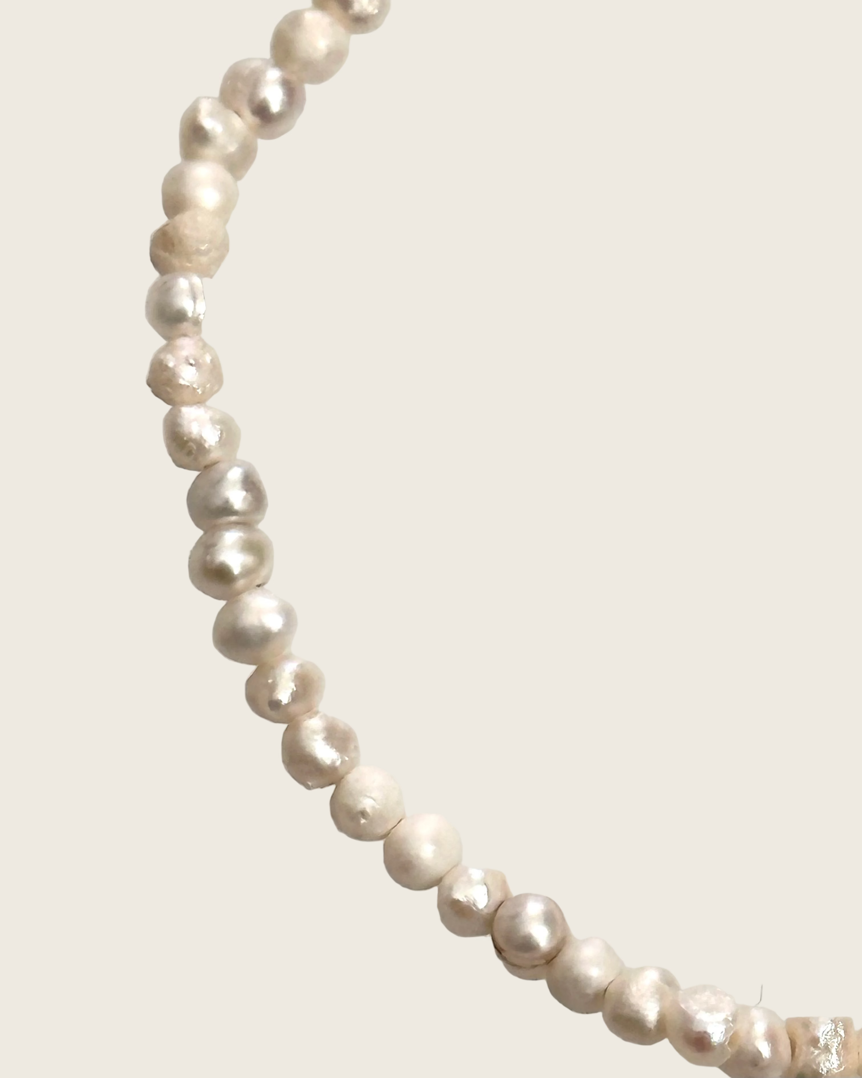 A strand of irregular, baroque-style freshwater pearls in a champagne beige color, arranged in a curved line against a plain light gray background.