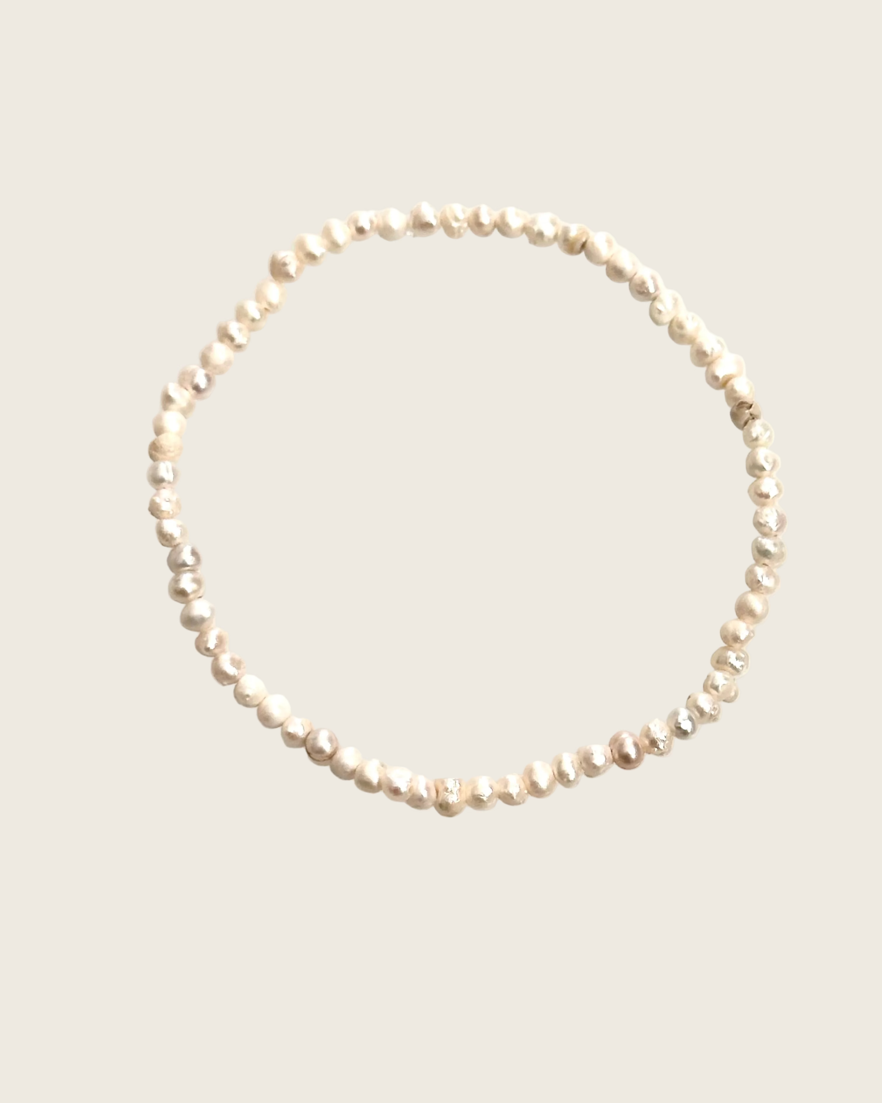 A single strand of irregular, lustrous pearl-like beads arranged in a loose circle on a plain white background.