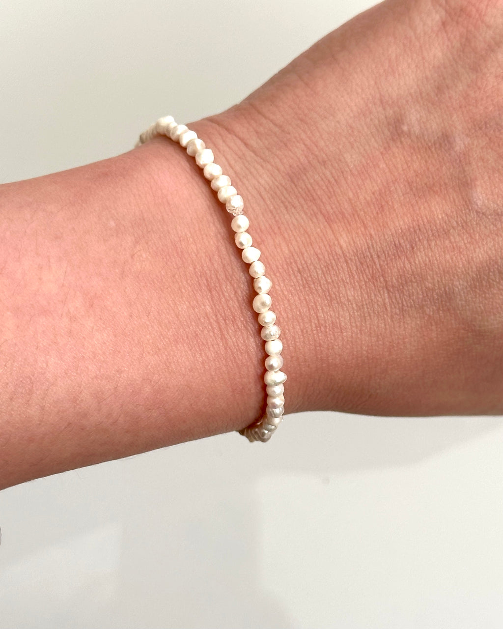 A delicate beaded bracelet made of small, irregular cream-colored pearls, shown worn on a person's wrist against a plain light background.