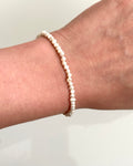 A delicate beaded bracelet made of small, irregular cream-colored pearls, shown worn on a person's wrist against a plain light background.