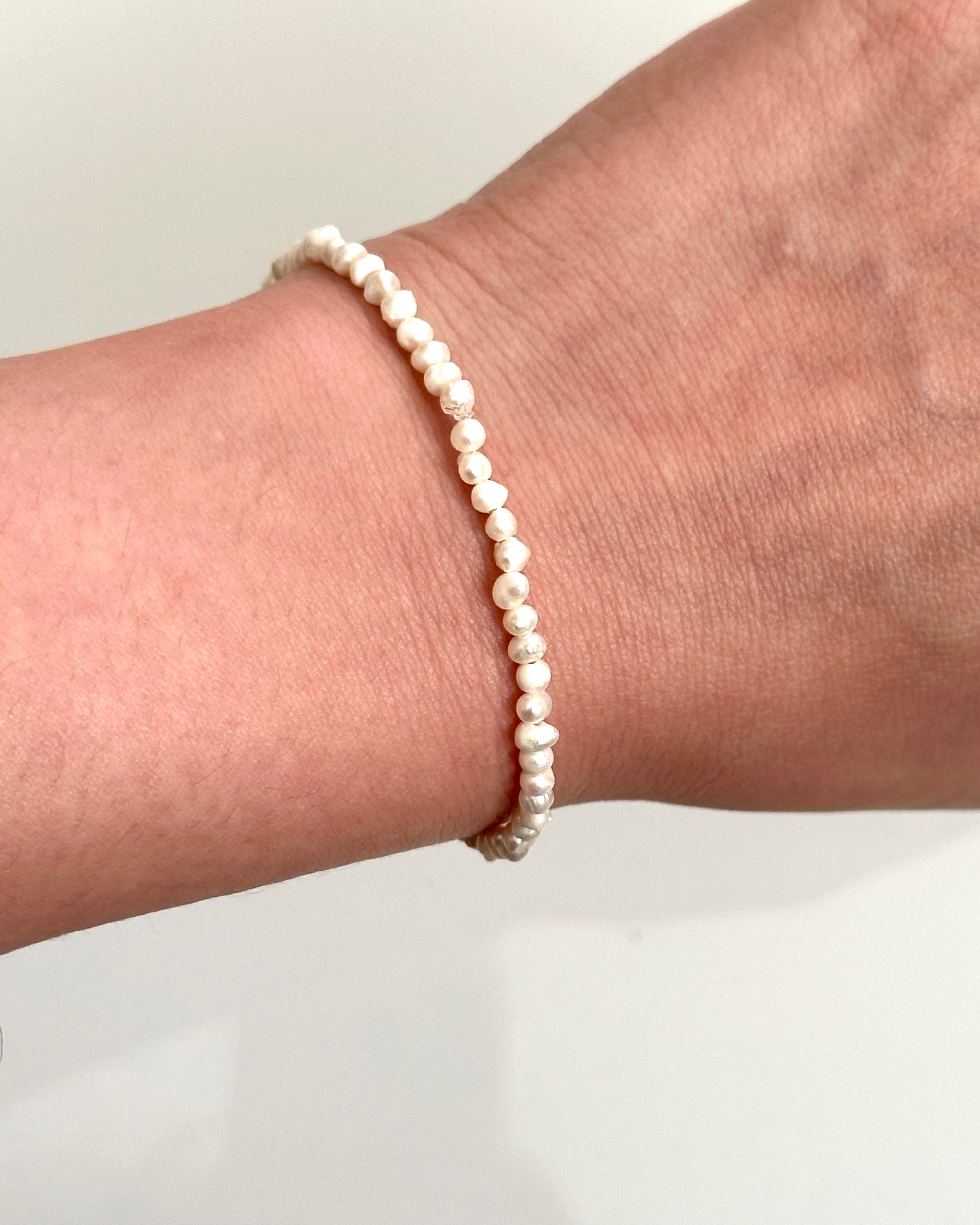 A delicate beaded bracelet made of small, irregular cream-colored pearls, shown worn on a person's wrist against a plain light background.