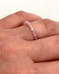 A close-up of a hand wearing a delicate beaded ring made of small, translucent light pink beads.