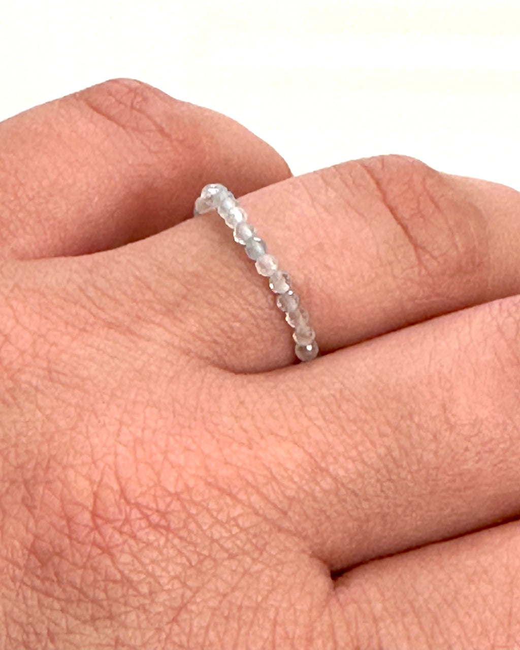 A delicate beaded ring made of small, faceted clear stones worn on a person's finger, shown against a plain white background.